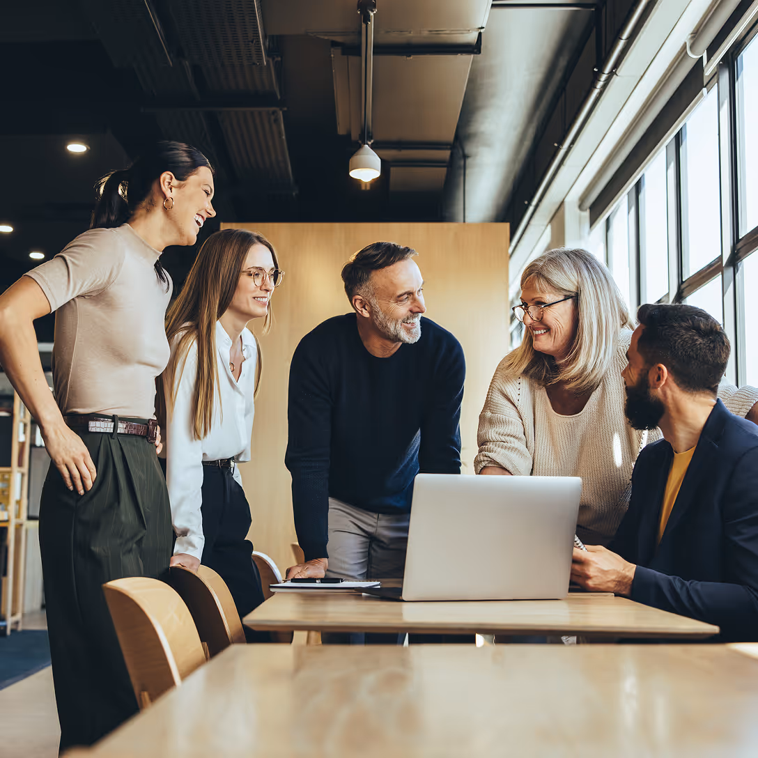 Fünf lächelnde Kollegen von Expertize stehen und sitzen um einen Tisch mit einem Laptop