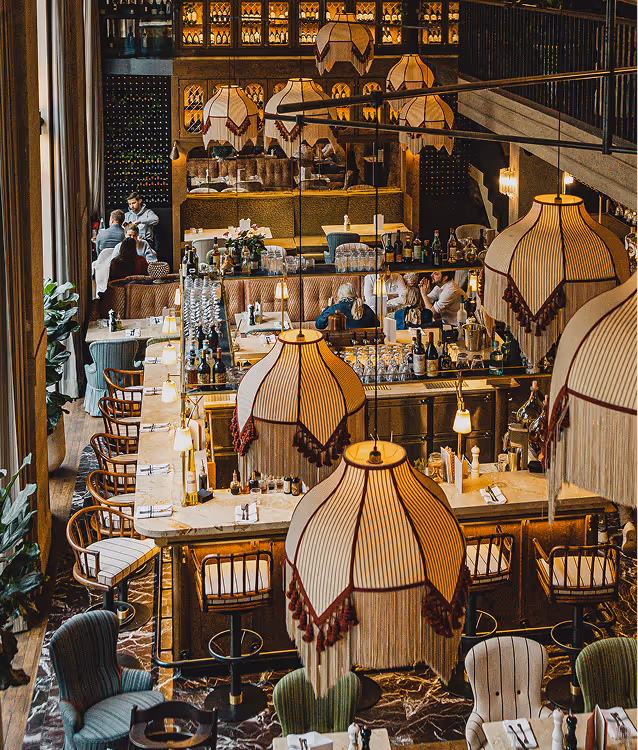 Stimmungsvolle Gesamtaufnahme des GIGI Restaurants in München mit imposanten Fransenlampen, offener Bar, eleganten Sitzbereichen und stilvoller Lichtinszenierung – italienisches Flair auf zwei Ebenen.