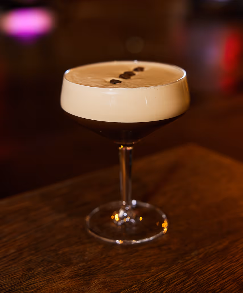 Espresso-Martini auf einem Holztisch im Italian Shot Glockenbach mit unscharfen Lichtern im Hintergrund.