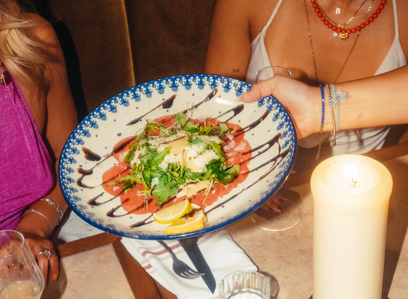 Servieren eines Carpaccio-Tellers im Italian Shot Glockenbach, umgeben von Gästen und Kerzenschein.