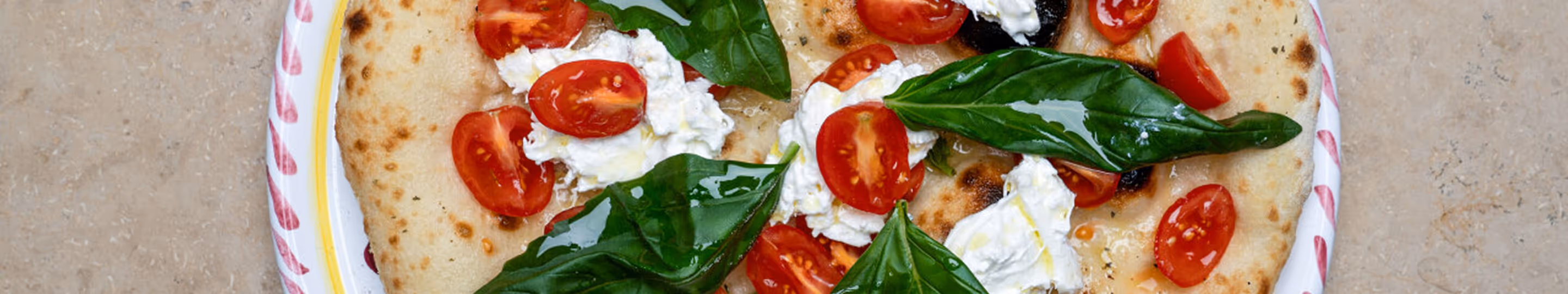 Pizza mit Tomaten, Burrata und Basilikum auf handbemaltem Teller im Italian Shot Glockenbach.