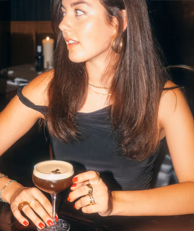 Frau im Italian Shot Glockenbach mit Espresso Martini, sitzend im warm beleuchteten Restaurantambiente.