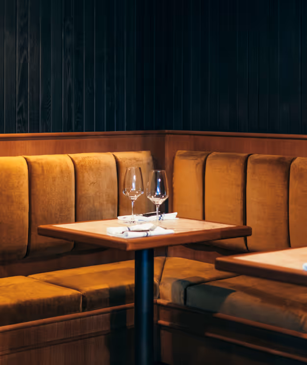 Sitzbereich im Italian Shot Glockenbach mit ockerfarbenen Samtbänken, gedeckten Tischen und Weingläsern.