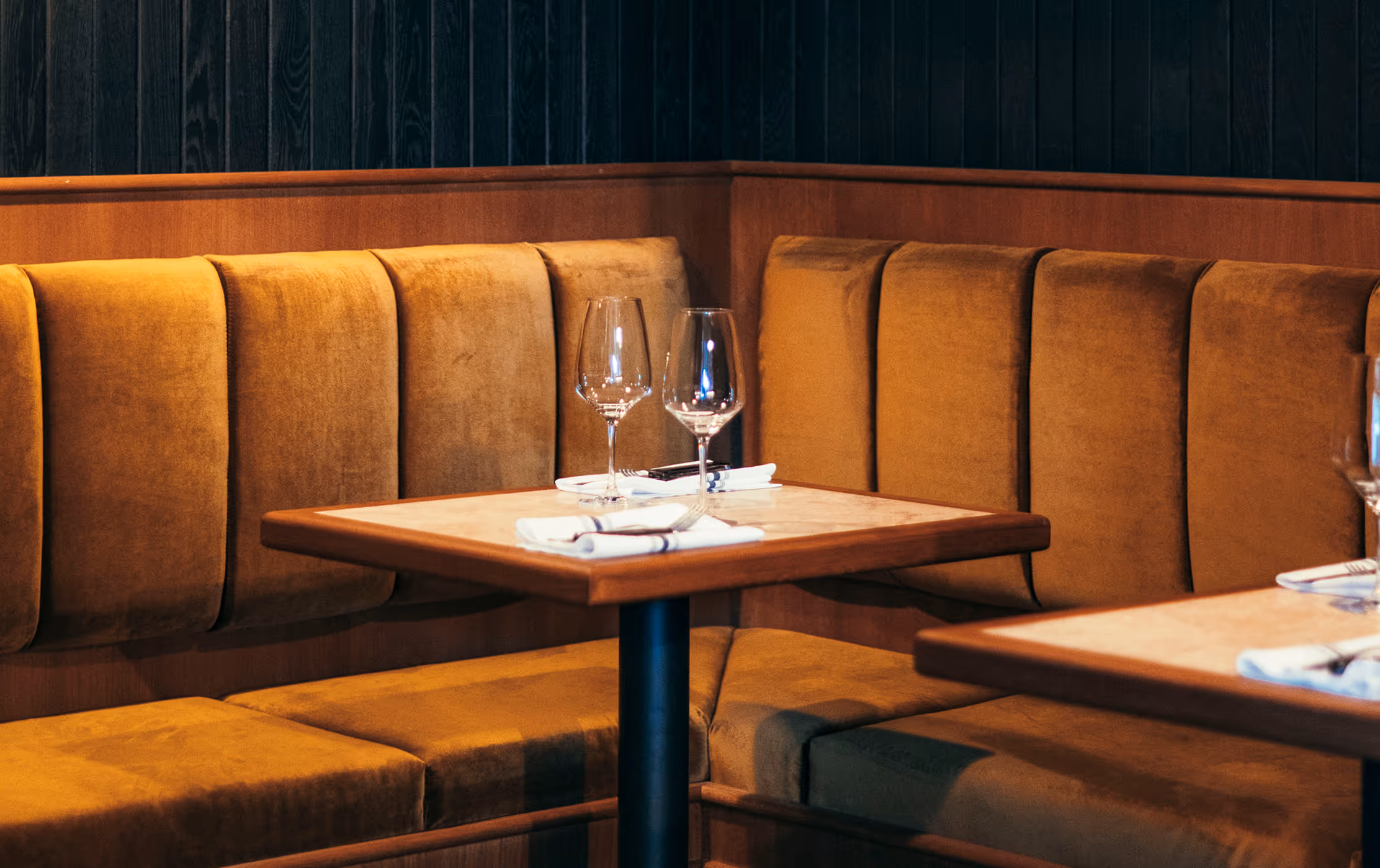 Sitzbereich im Italian Shot Glockenbach mit ockerfarbenen Samtbänken, gedeckten Tischen und Weingläsern.