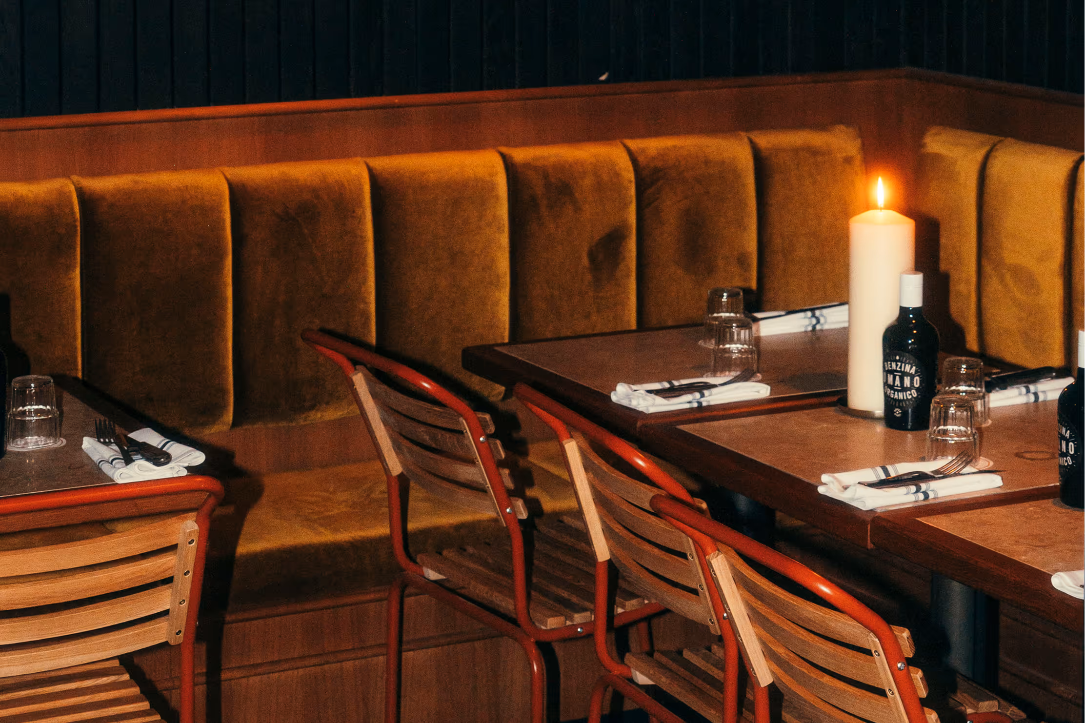 Restaurantbereich des Italian Shot Glockenbach mit Polsterbänken in Ocker, Holztischen und Kerzen.