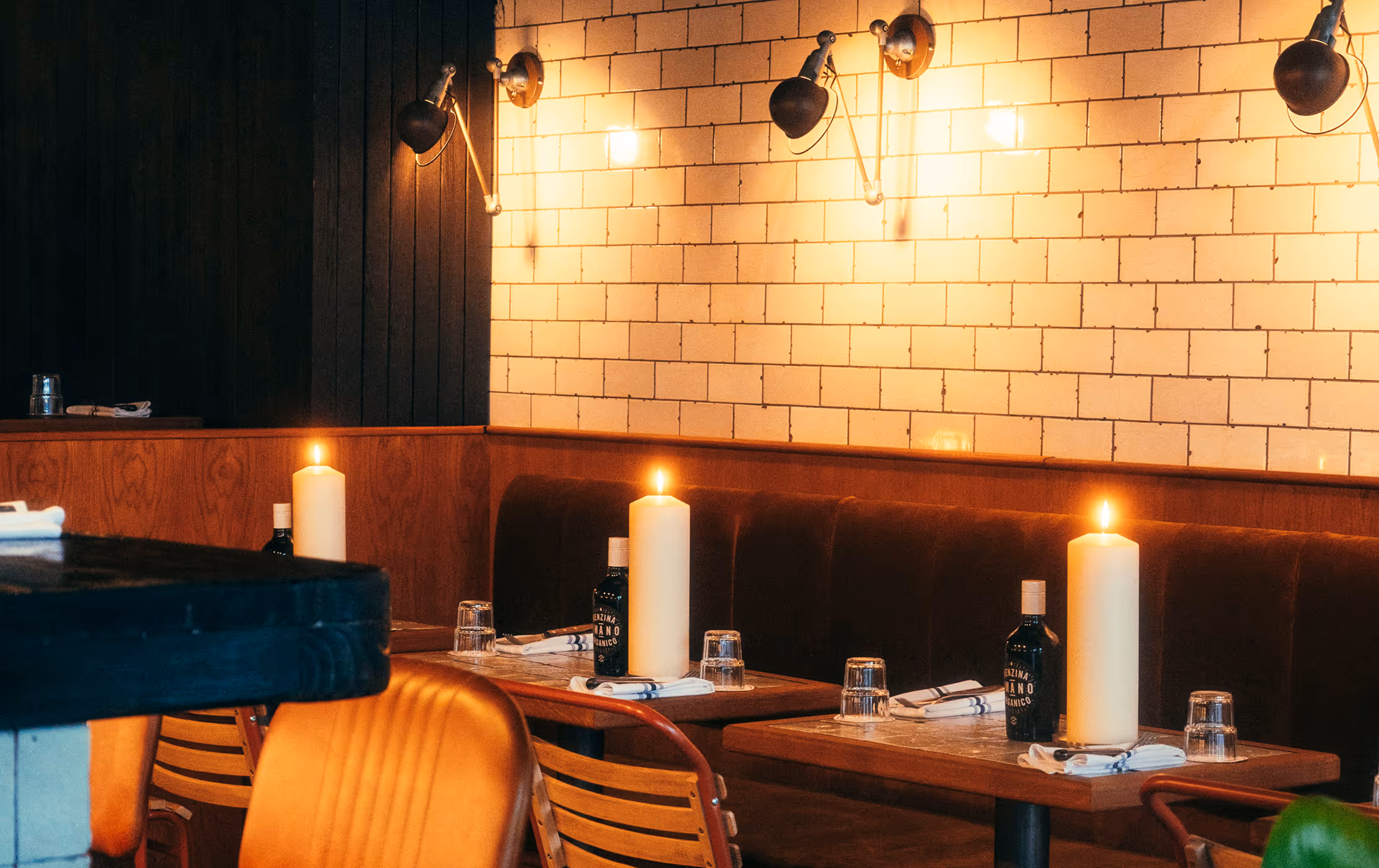 Gemütlicher Restaurantbereich im Italian Shot Glockenbach mit warmem Kerzenlicht, Polsterbänken, Holztischen und Wandfliesen.