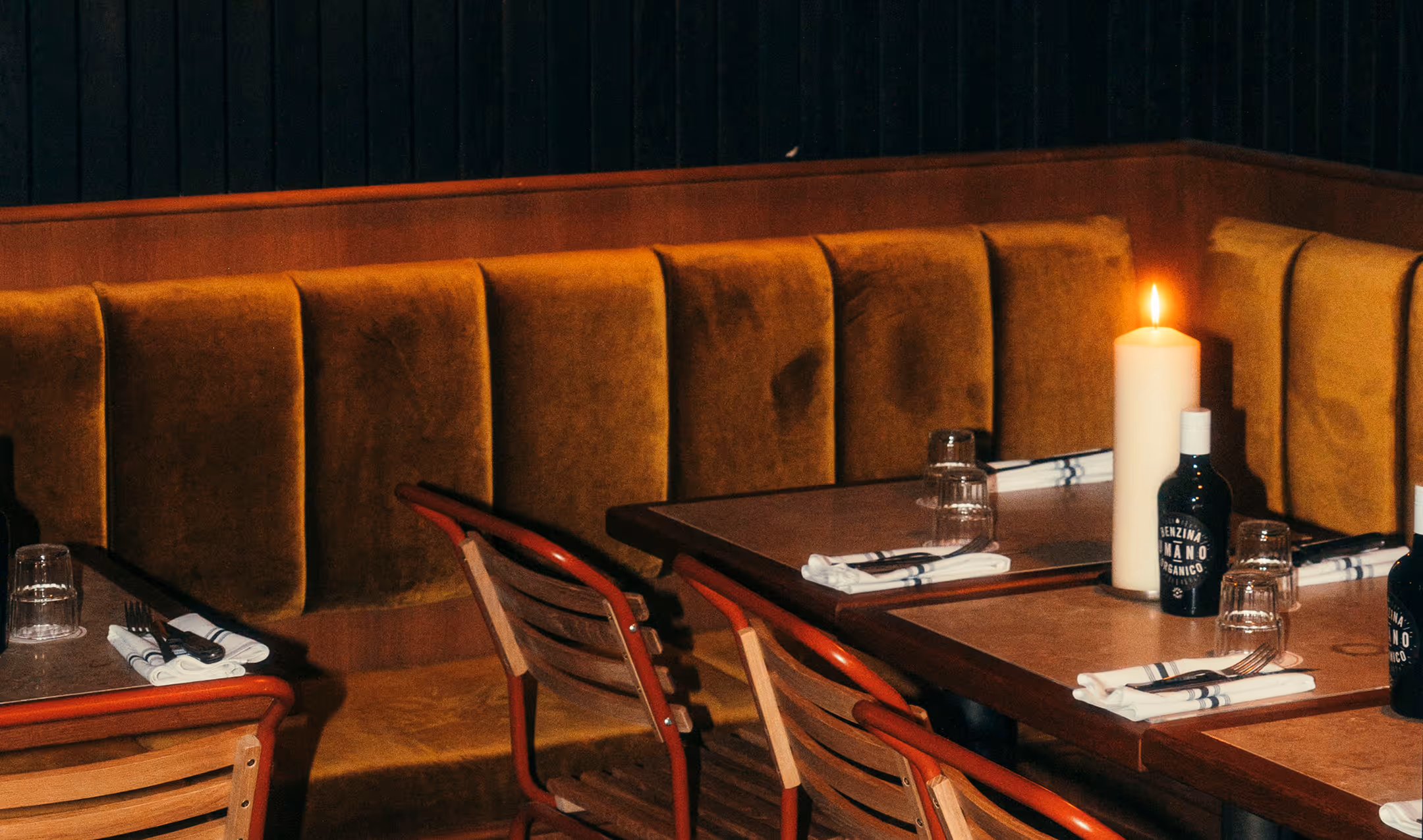Restaurantbereich des Italian Shot Glockenbach mit Polsterbänken in Ocker, Holztischen und Kerzen.