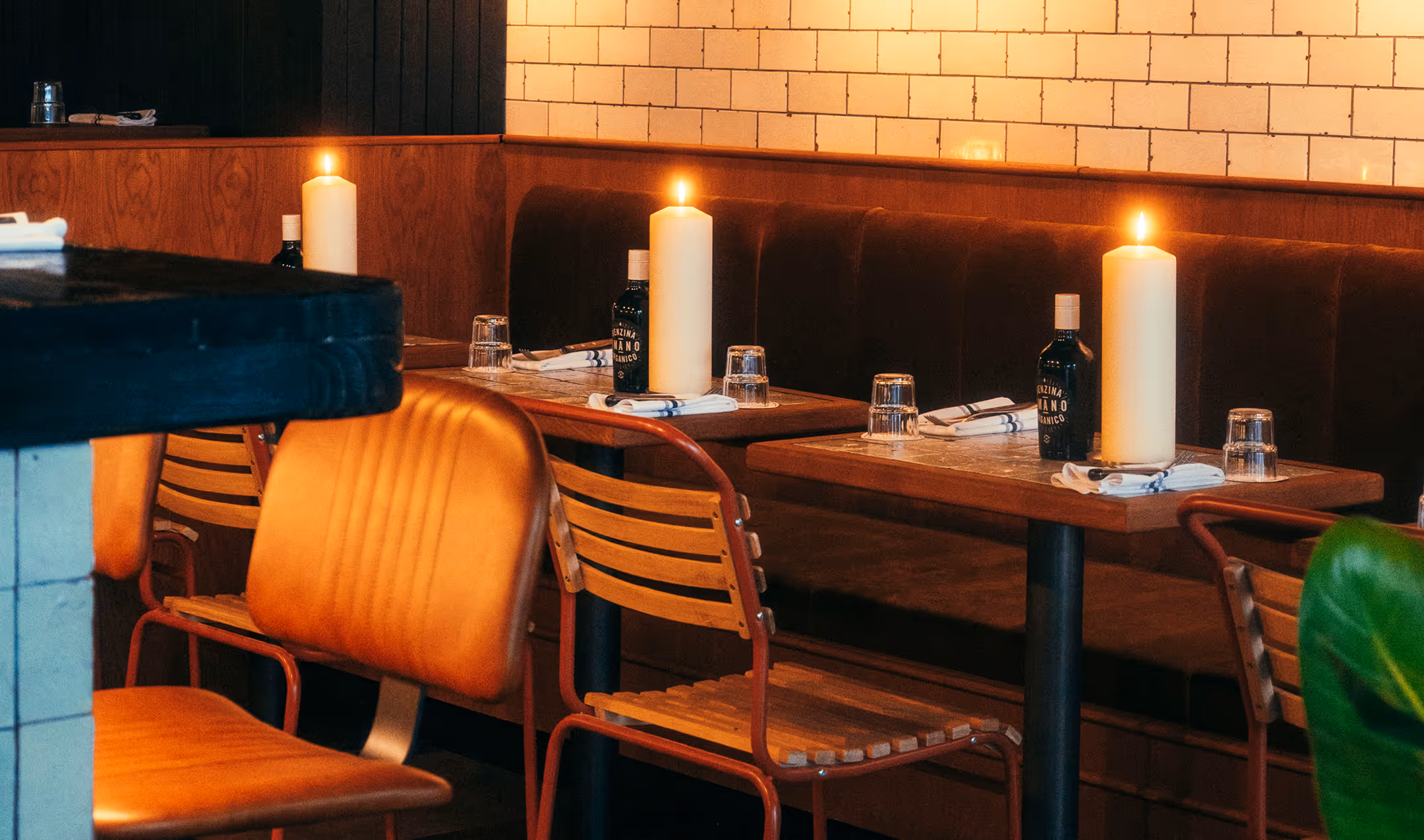 Gemütlicher Restaurantbereich im Italian Shot Glockenbach mit warmem Kerzenlicht, Polsterbänken, Holztischen und Wandfliesen.