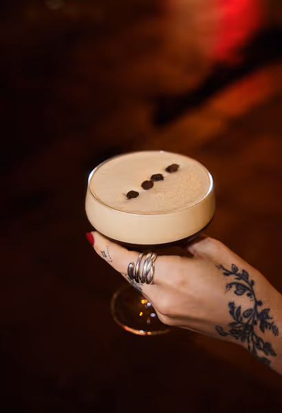 Espresso Martini wird im Italian Shot Maxvorstadt in einer Hand mit Schmuck und Handtattoos gehalten.