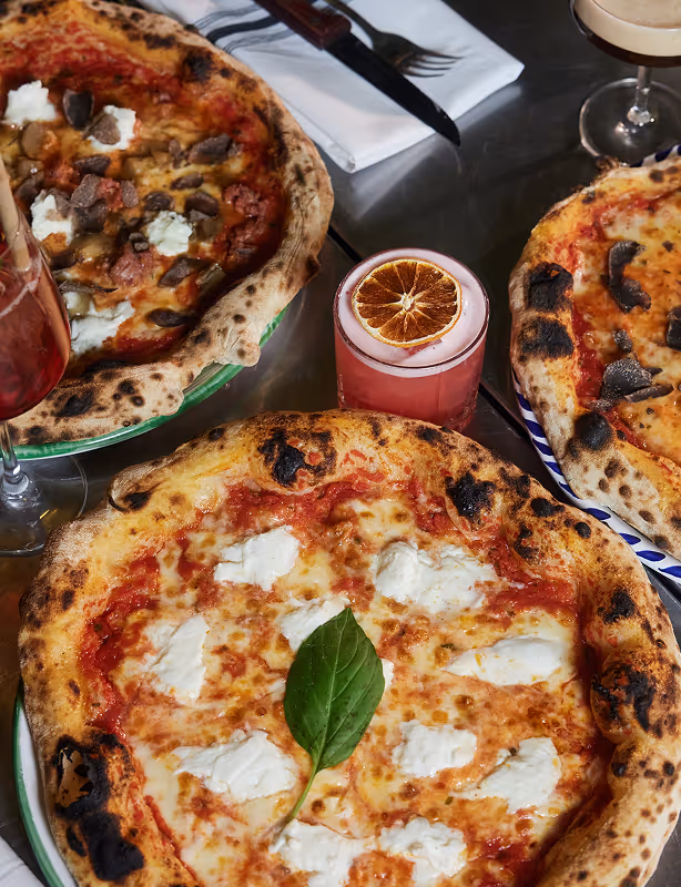 Drei neapolitanische Pizzen mit Cocktails und Olivenöl auf einem gedeckten Tisch im Italian Shot Maxvorstadt.