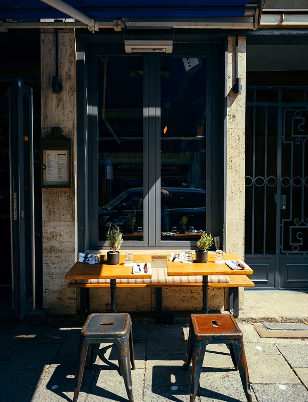 Zwei kleine Außentische mit Hockern vor dem Italian Shot Maxvorstadt, bereit für Gäste.