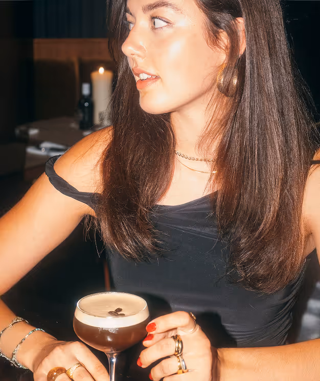 Frau im Italian Shot Maxvorstadt mit Espresso Martini, sitzend im warm beleuchteten Restaurantambiente.