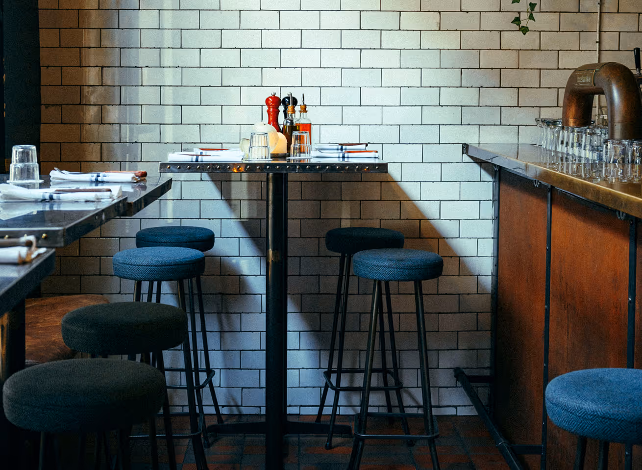 Hochtische und Barhocker im Italian Shot Maxvorstadt vor weiß gefliester Wand und großen Parmesanlaiben.