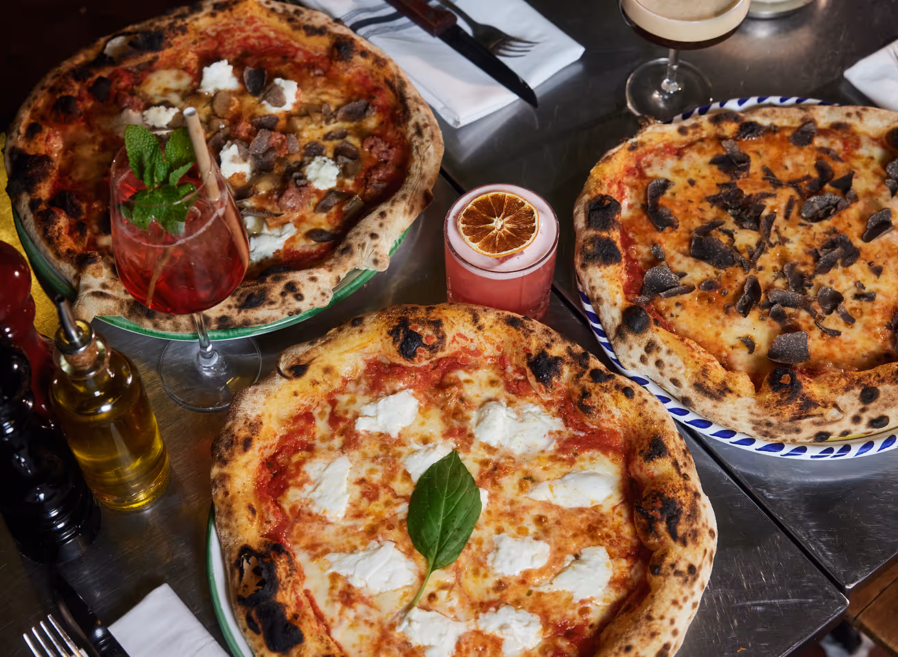 Drei neapolitanische Pizzen mit Cocktails und Olivenöl auf einem gedeckten Tisch im Italian Shot Maxvorstadt.