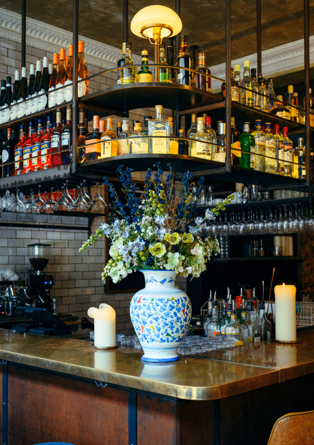 Barbereich im Italian Shot Maxvorstadt mit Blumenarrangement, Messingtheke und Regalen voller Spirituosen.