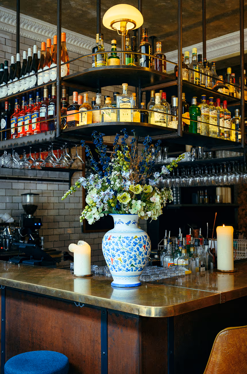 Barbereich im Italian Shot Maxvorstadt mit Blumenarrangement, Messingtheke und Regalen voller Spirituosen.