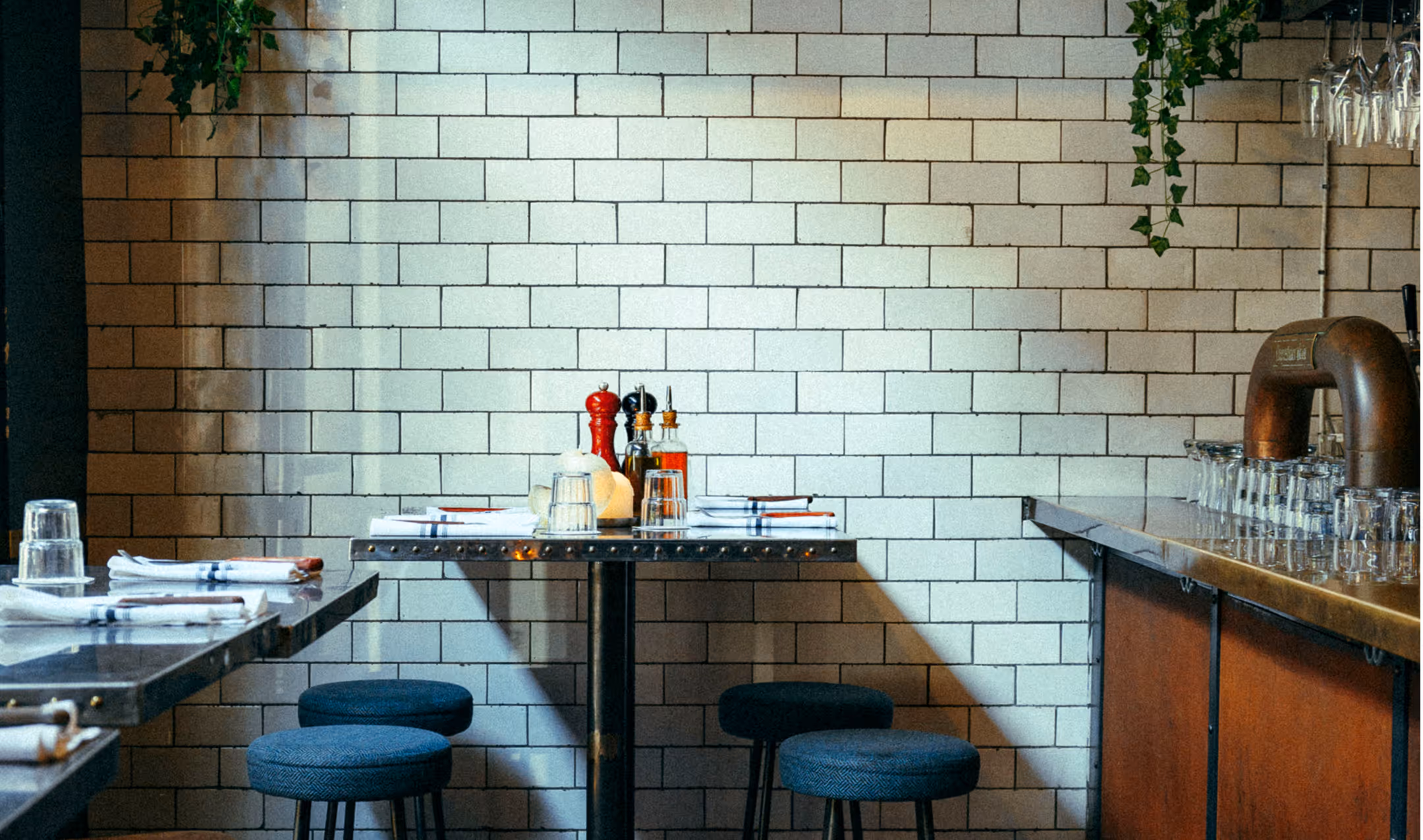 Hochtische und Barhocker im Italian Shot Maxvorstadt vor weiß gefliester Wand und großen Parmesanlaiben.