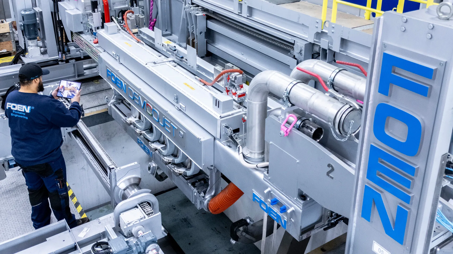Techniker bedient eine große industrielle Maschine mit dem Schriftzug FOEN in einer Produktionshalle.