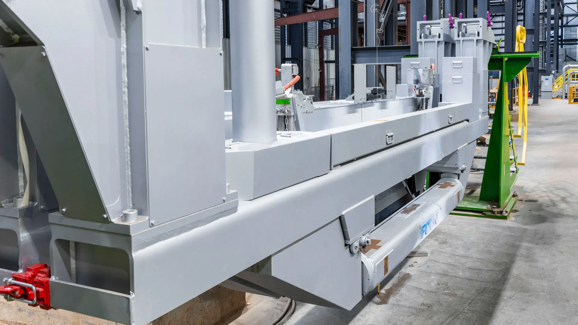 Große graue industrielle Maschine in einer Fabrikhalle mit Betonboden und Metallstrukturen.