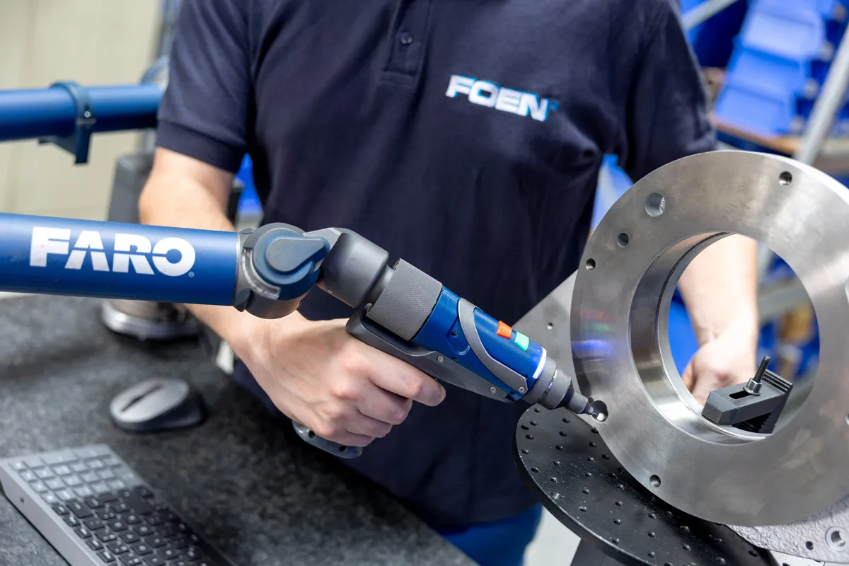 Person bedient ein blaues FARO-Messgerät zur 3D-Messung an einem metallischen, runden Werkstück.