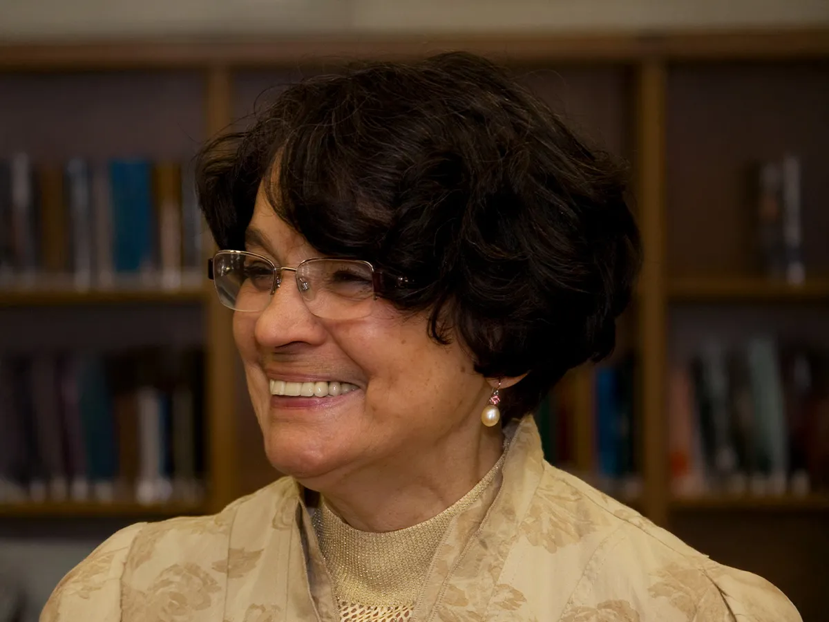 Portrait of a smiling elderly woman wearing glasses and short dark hair in front of bookshelves.