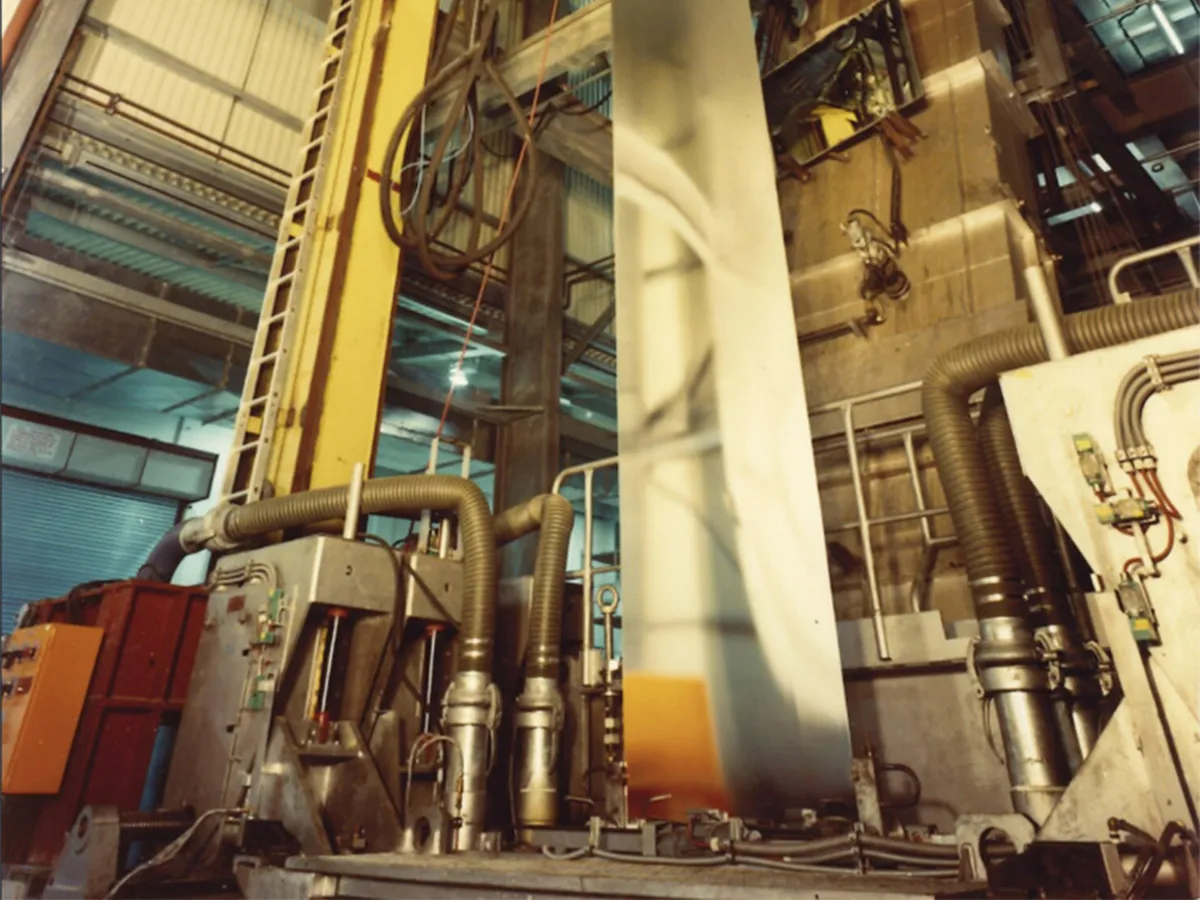 Industrial manufacturing plant with large metal pipes and machines in a factory environment.