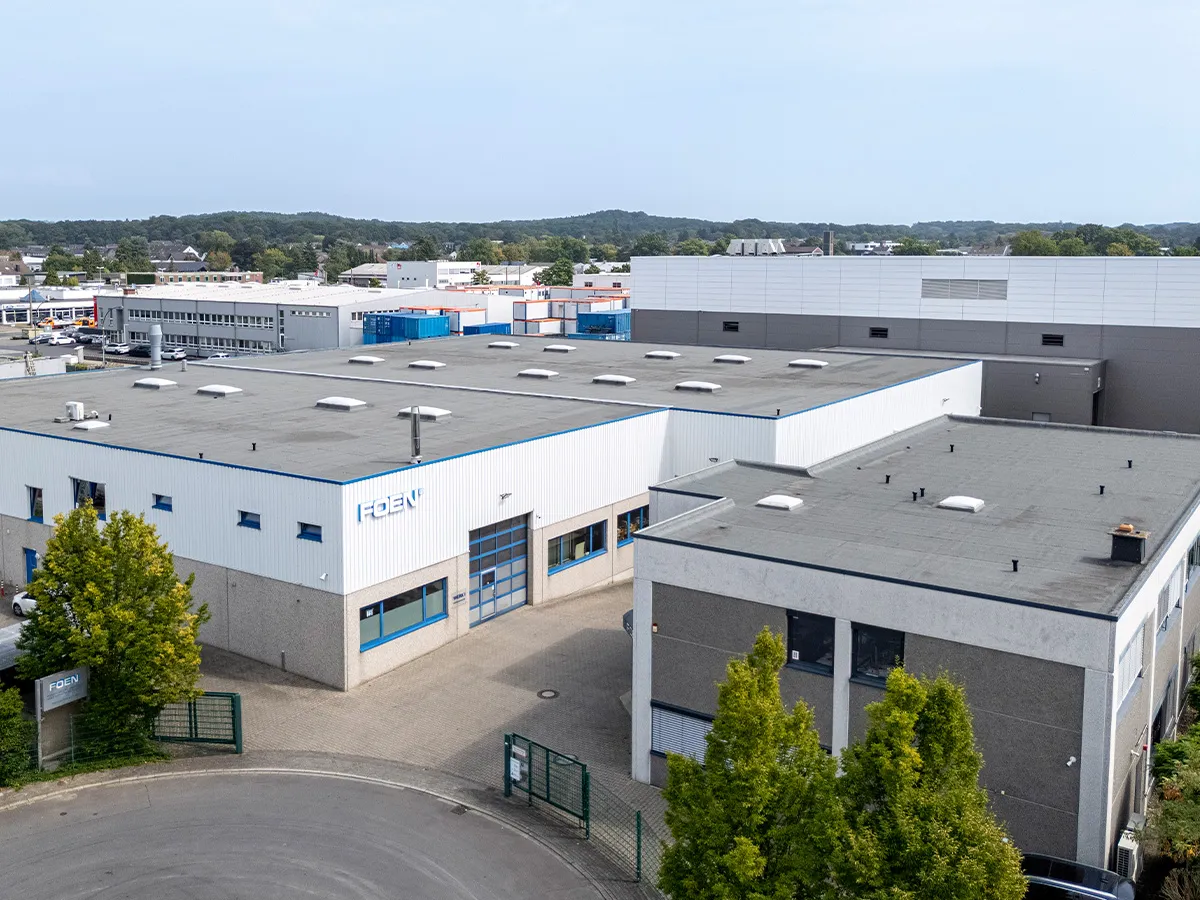 Industrial building with the FOEN logo on the façade, surrounded by trees and other factory buildings in the background.