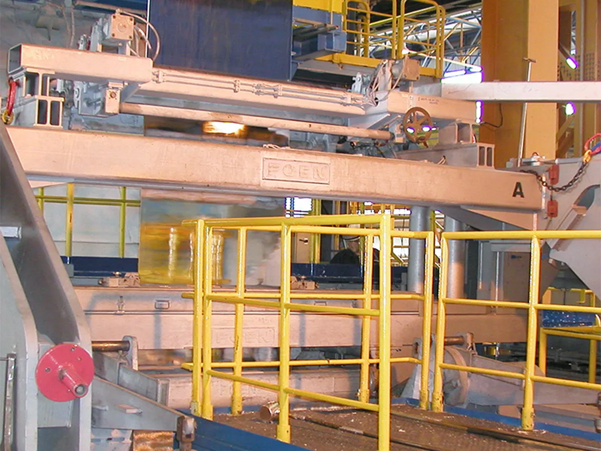 Industrial machine with yellow safety railings and conveyor belts in a factory environment.