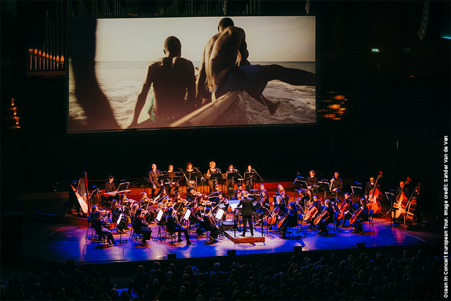 Ocean in Concert on a large screen with an orchestra playing in front of the screen