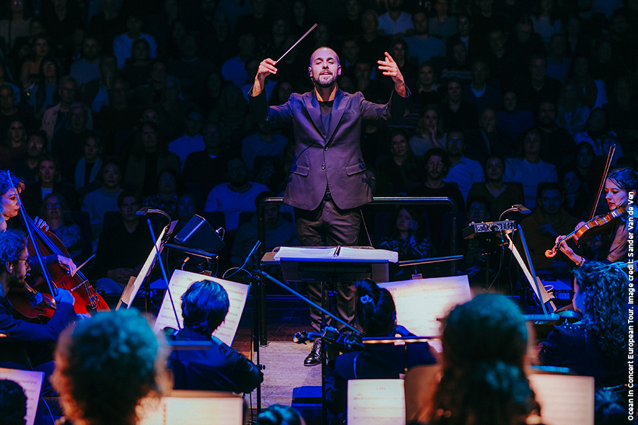A conductor and orchestra in front of a live audience