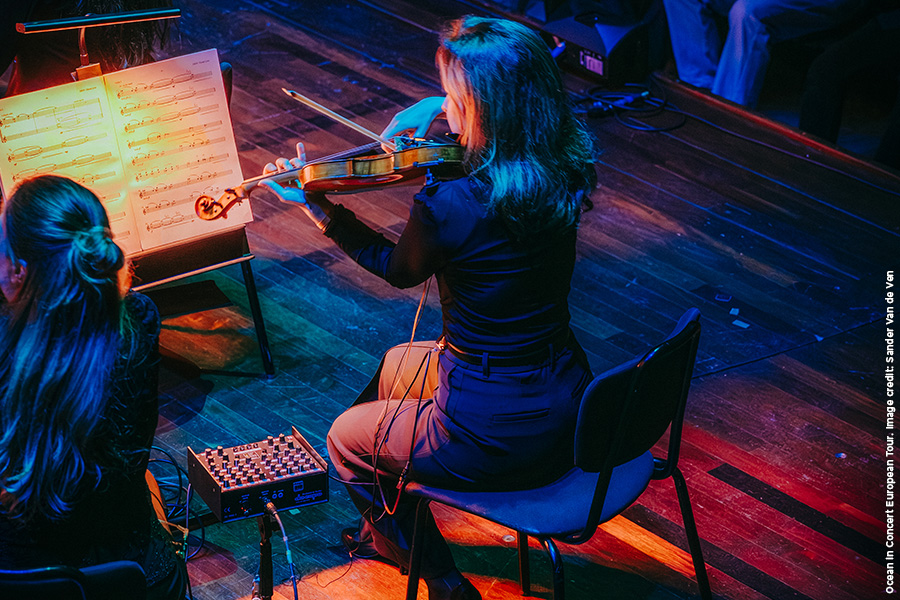 A violinist sitting in front of amusic stand playing on stage