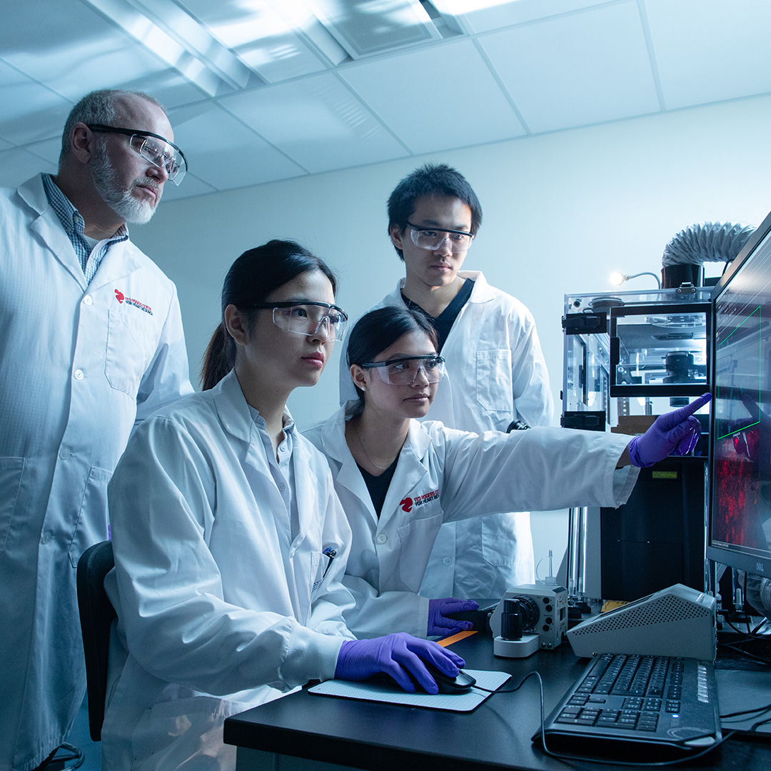 Group of individuals in lab coats, looking at a computer monitor