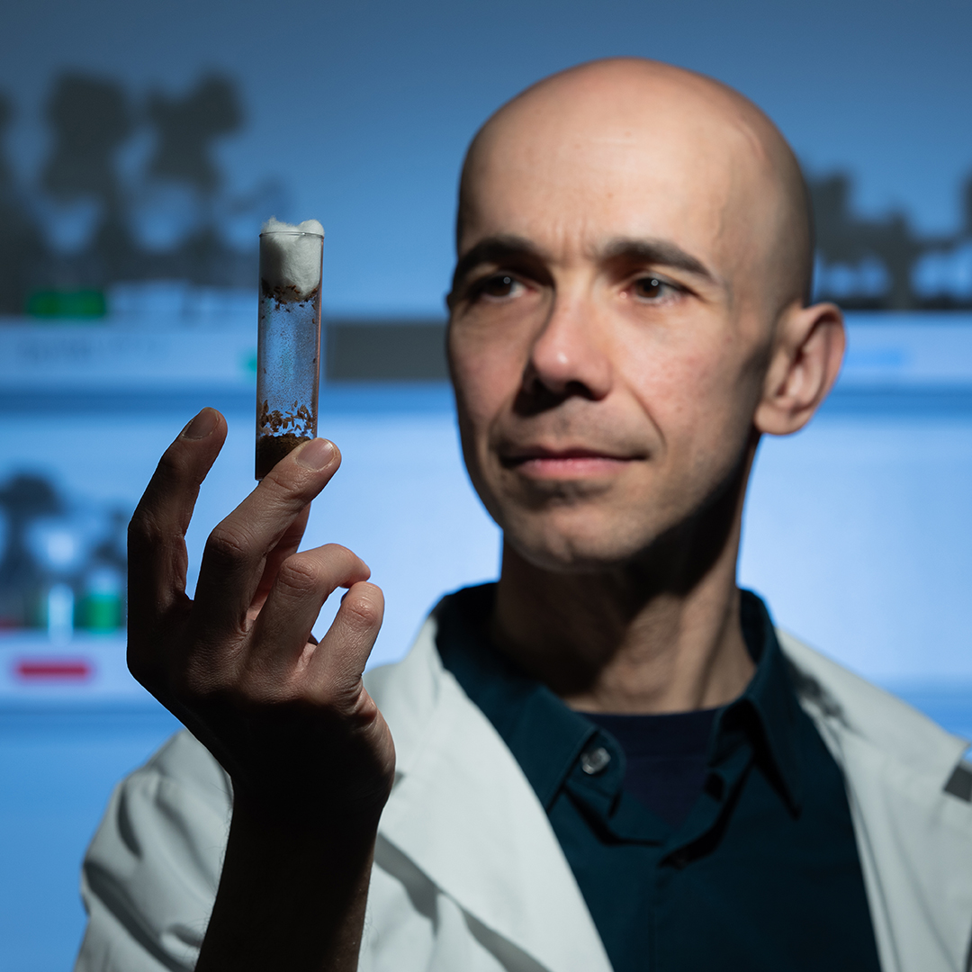 Scientist in a lab coat holding and examining a test tube.