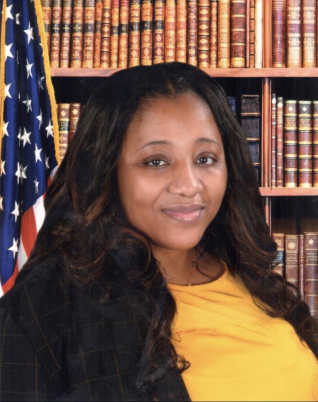 Ms. Williams official staff portrait with American flag and bookshelf