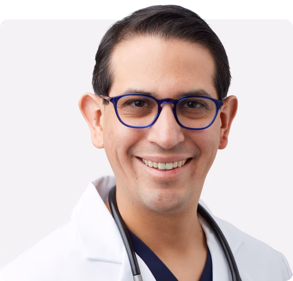 Portrait of Dr. Carlos Quesada wearing a white medical coat and glasses.