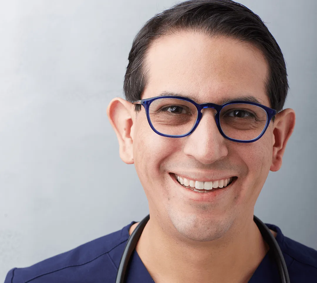 Dr. Carlos Quesada with a stethoscope, smiling in his medical office.