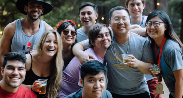 Diverse group of young adults smiling and posing together outdoors with drinks in hand happily.