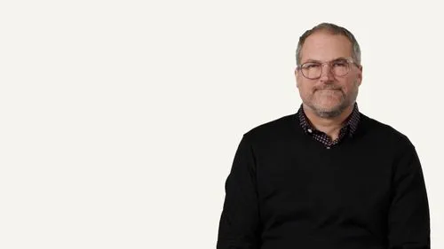 Man in black sweater and glasses looking directly at camera on white background.