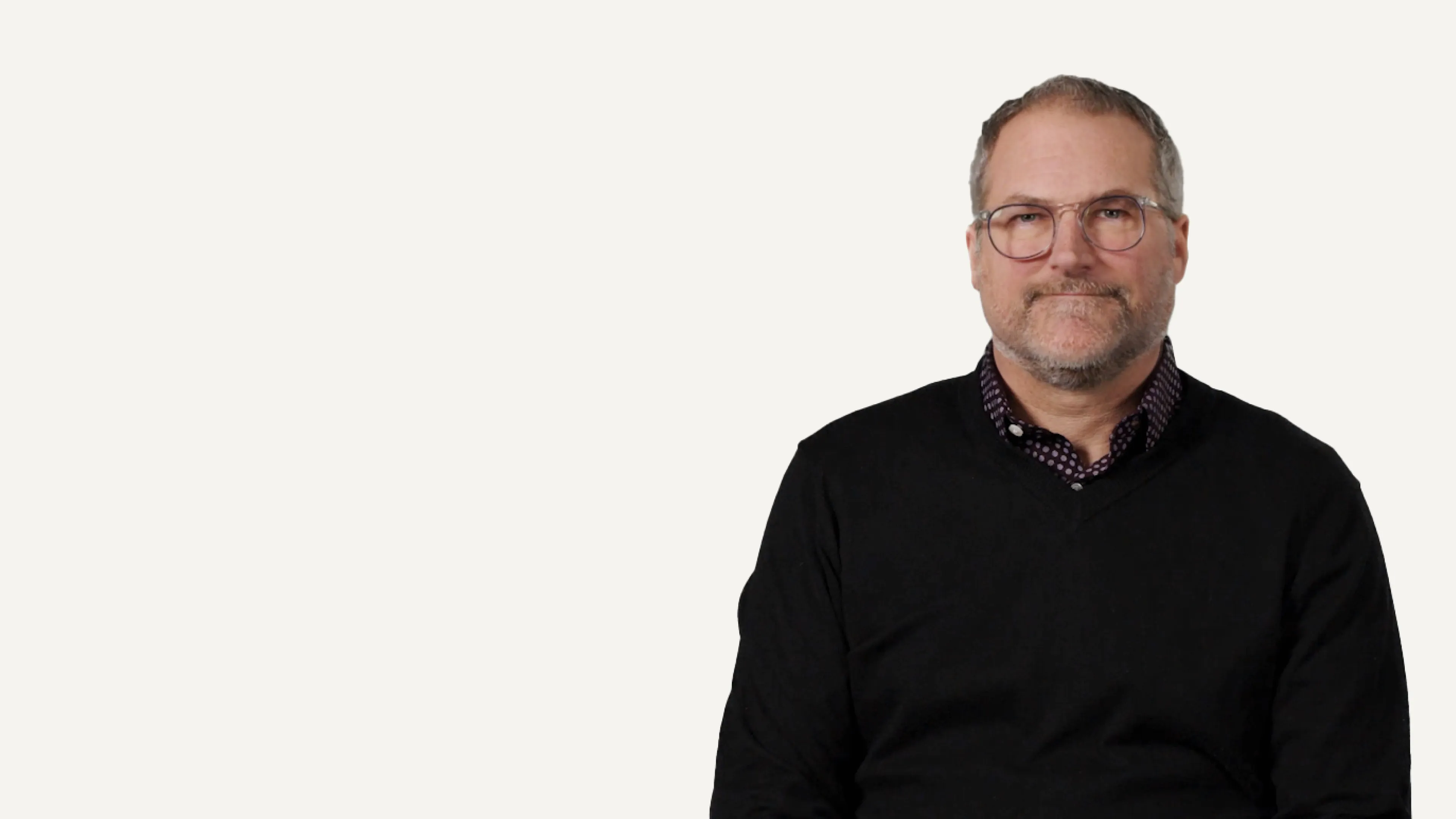 Man in black sweater and glasses looking directly at camera on white background.