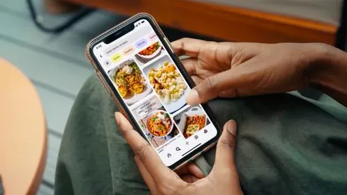 Person holding phone with pasta recipes on screen, showing healthy and quick meal options.