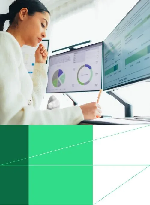 Woman analyzes data on dual monitors with pie charts and graphs for business insights.