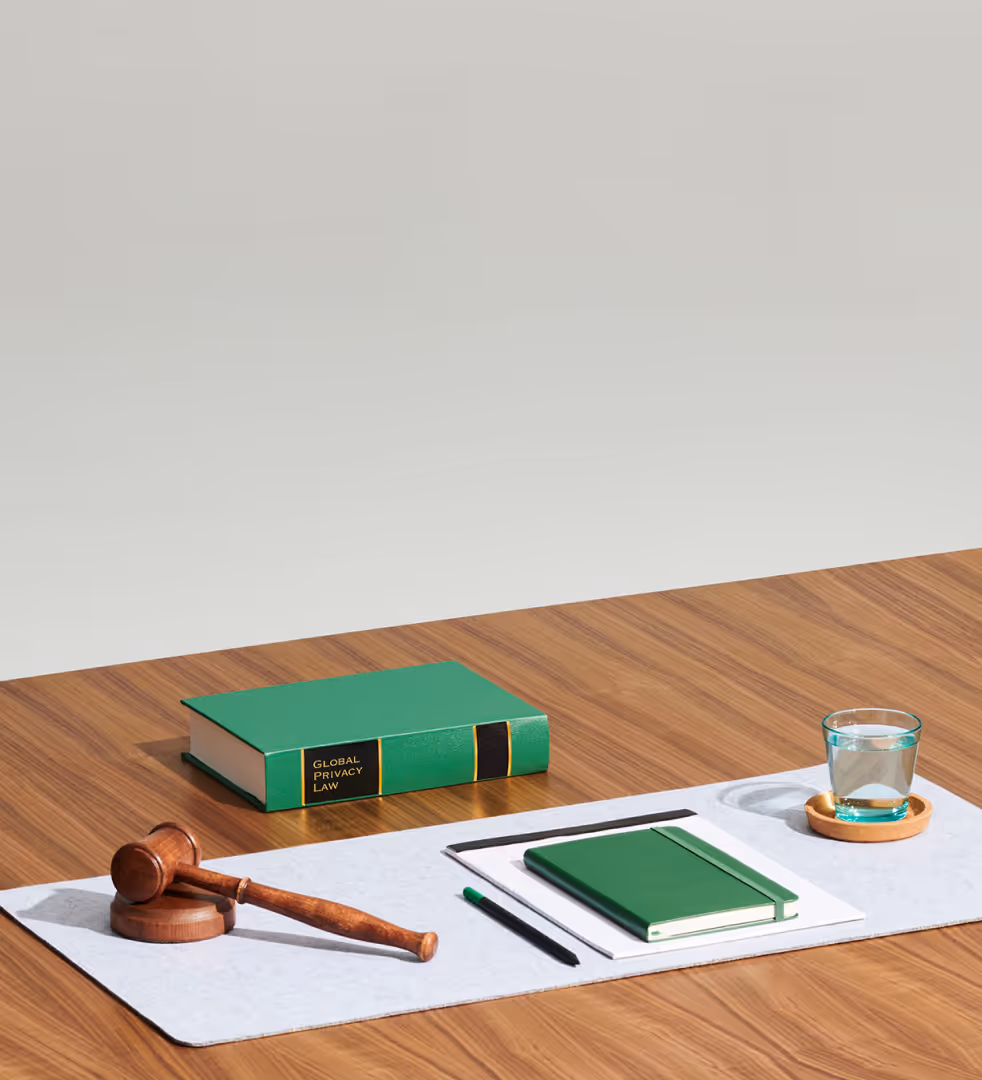 Wooden desk with law book, gavel, notebook, pen, and glass of water on white papers.