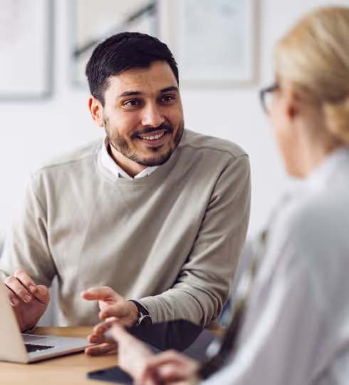 Man and woman engaged in discussion at desk with laptop in office setting.