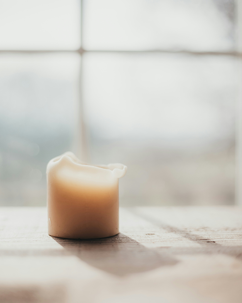 A candle on a windowsill that is partially melted.