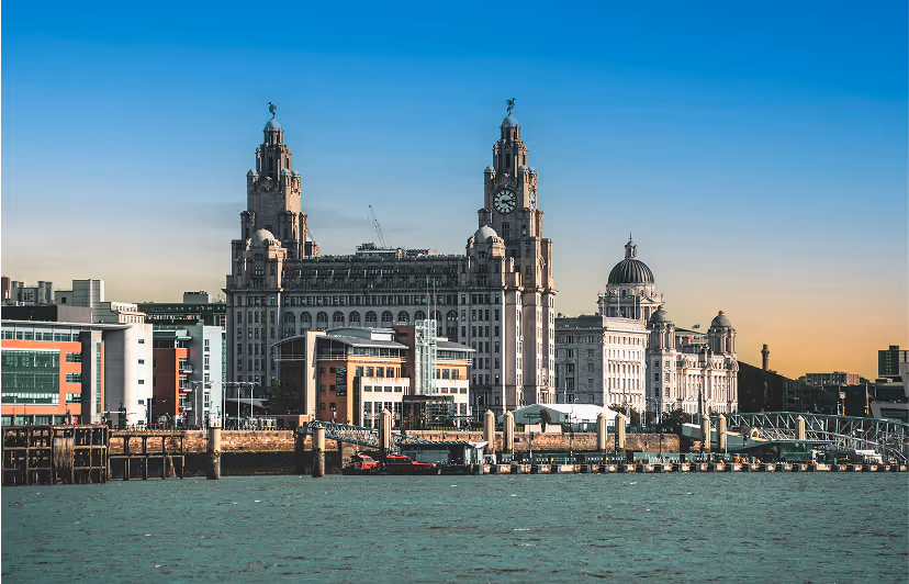 Waterfront view of Liverpool's Royal Liver Building and surrounding historic architecture under a clear blue sky.