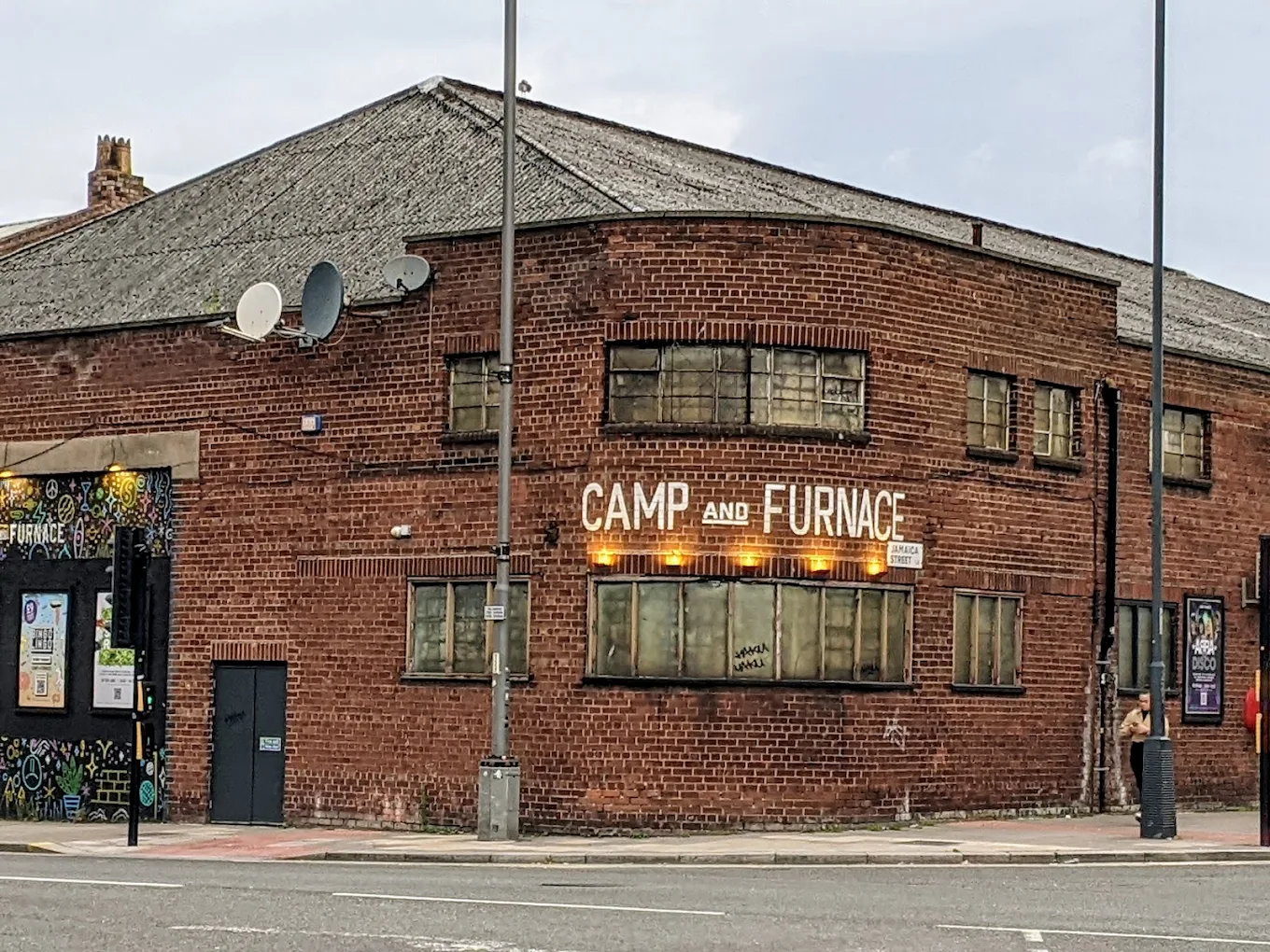 Brick building on a street corner with sign reading 'Camp and Furnace' illuminated by yellow lights.
