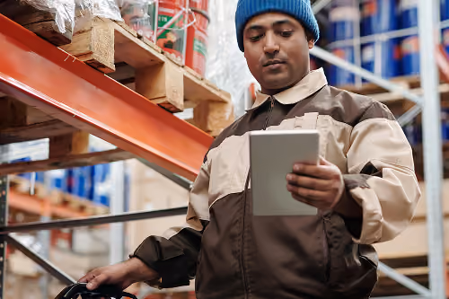 Inventory support worker reviewing stock levels and data on a tablet in a distribution center.