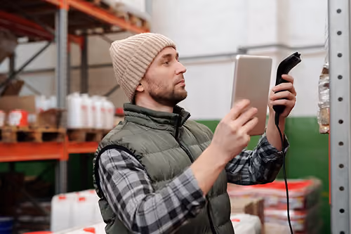 Order picker using a handheld scanner to check inventory on warehouse shelves.