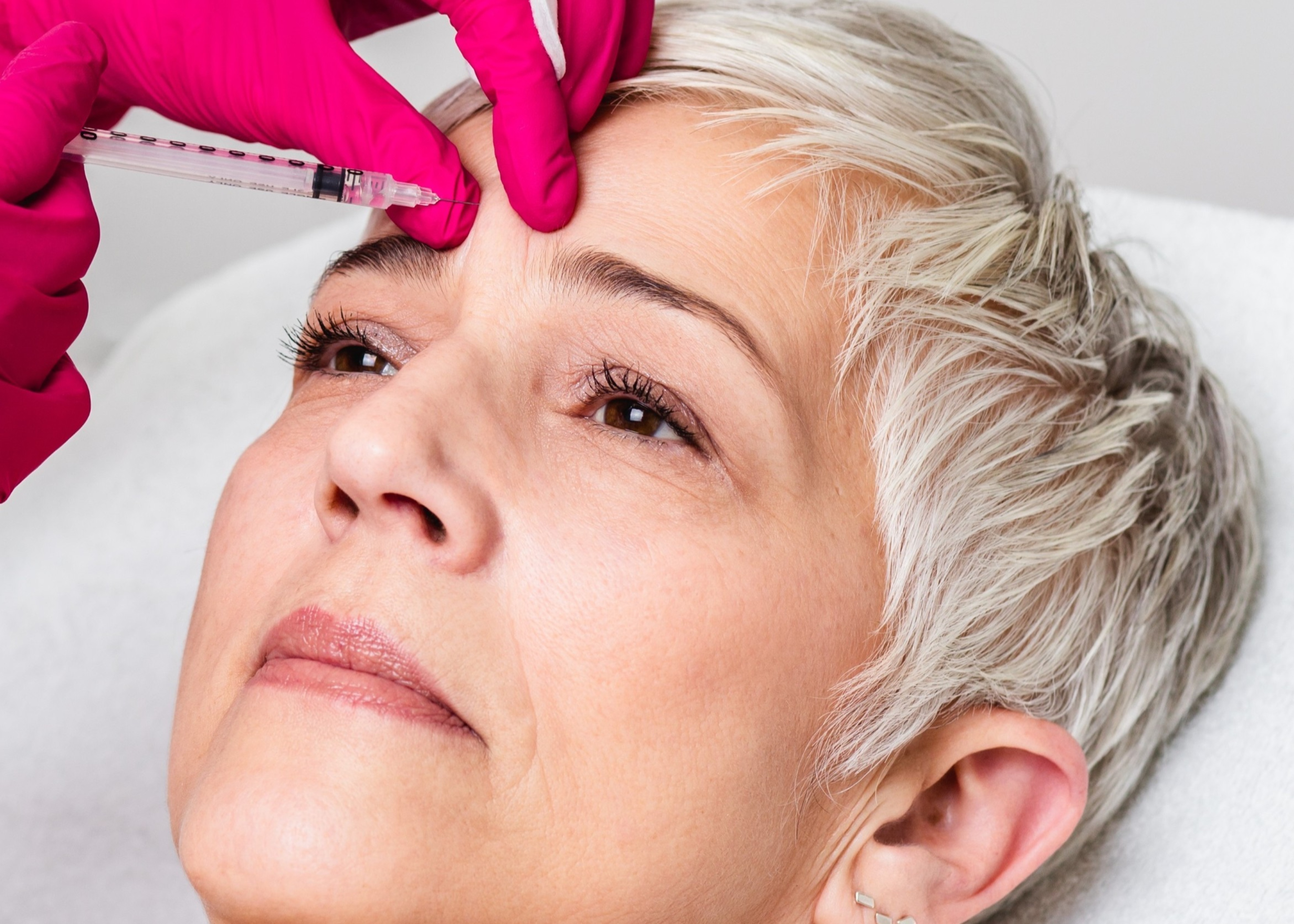 A woman getting her eyebrows brushed by a doctor.