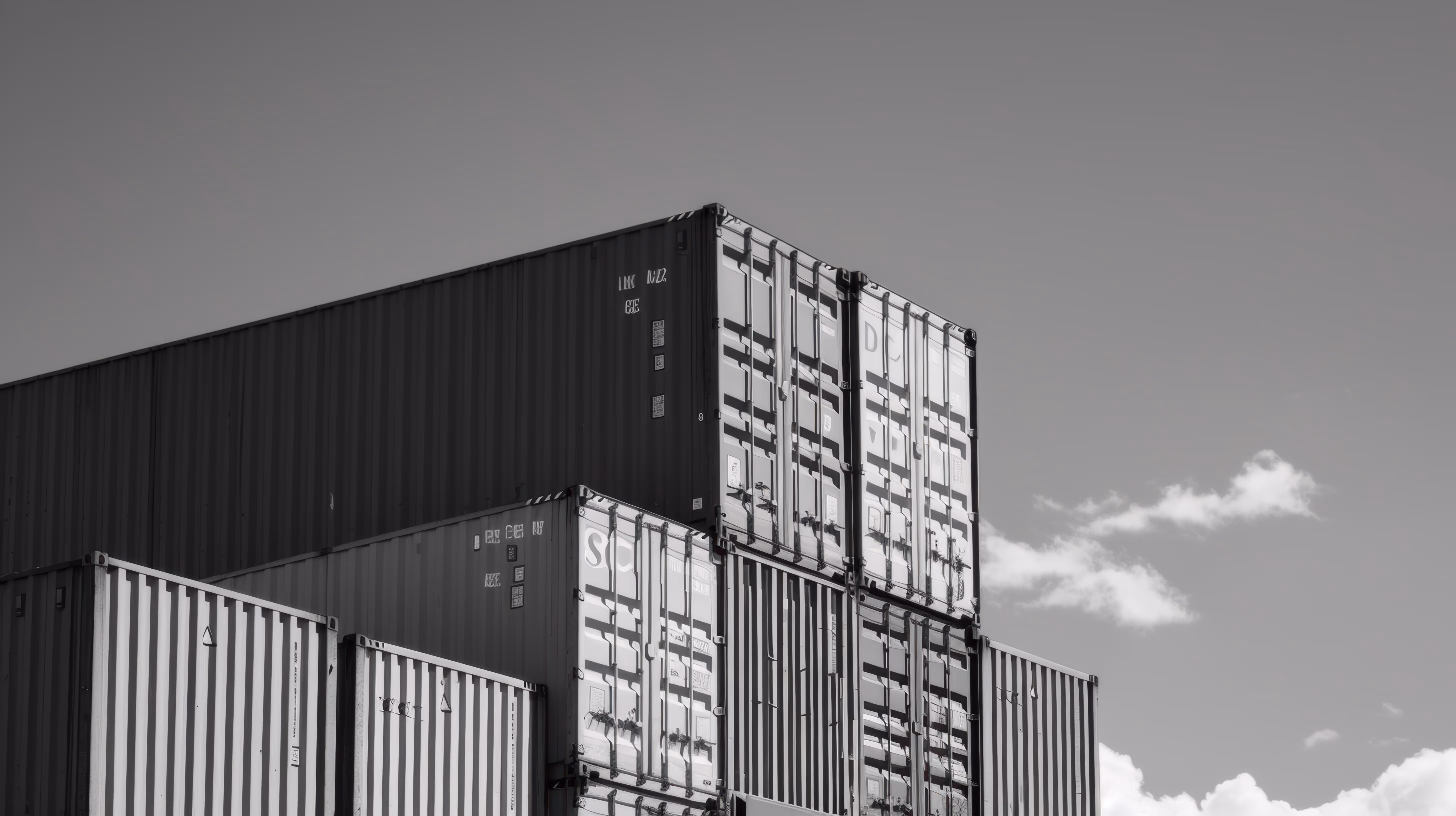 Stacked shipping containers in black and white against cloudy sky